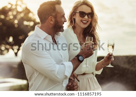Smiling man and woman enjoying a glass of wine outdoors. Happy couple with a glass of wine sitting outdoors.