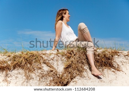 Pretty woman sitting on sand dune against the bright sky background