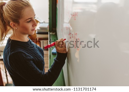 Close up of female student writing an equation on white board in classroom. Girl writing on board during maths class.