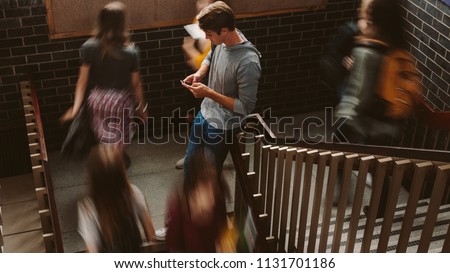 Young man standing on the staircase in college with girls walking by. Students on steps of college campus.
