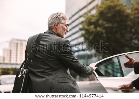 Mature businessman getting into a cab with driver opening door. Businessman entering a taxi on city street.