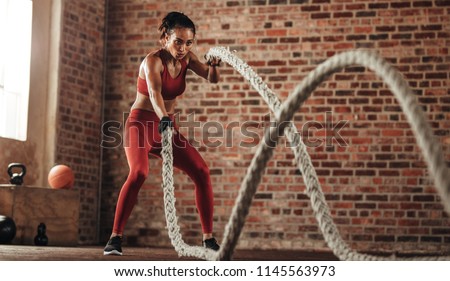 Athlete moving the ropes in wave motion as part of fat burning workout in fitness studio. Sportswoman exercising with battling ropes at gym.