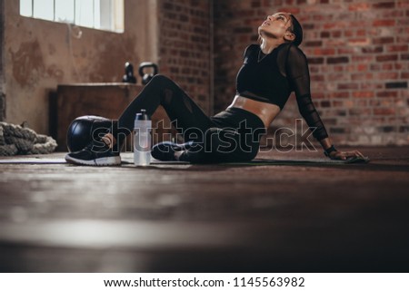 Tired woman having rest after workout. Tired and exhausted female athlete sitting on floor at gym with a water bottle.