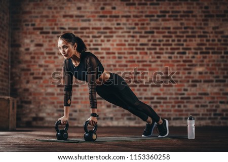 Fitness woman doing pushups with kettle bell at gym. Female athlete doing cross training at gym.