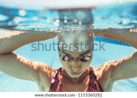 Underwater shot of woman inside swimming pool. Female swimmer in swim cap and goggles inside pool.