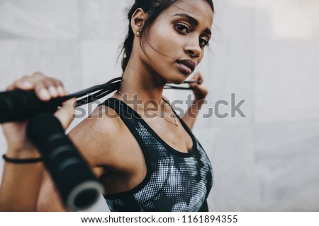 Close up of a woman athlete in fitness clothes during her workout holding a skipping rope behind her neck.
