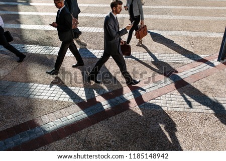 Business people commuting to office in the morning carrying office bags and using mobile phones. Businessmen in a hurry to reach office walking on city street using their mobile phone.