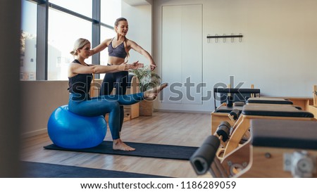 Fitness woman doing pilates workout sitting on an exercise ball at gym. Fitness trainer guiding a woman in pilates training.