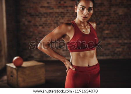 Woman standing after workout at gym. Gym woman in red sports clothing looking at camera.