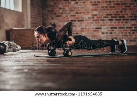 Fit female doing intense core workout in gym. Young woman doing push up exercise on fitness mat in health club.
