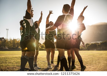 Rugby players celebrating a win at the sports field. Rugby team with hands raised and screaming after victory.