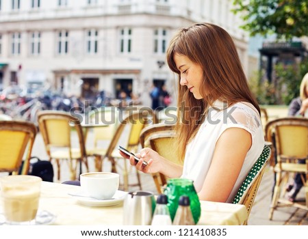 Attractive woman in a street cafe reading a text message from her phone