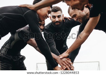 Low angle view of footballers talking about the game plan standing in a huddle. Soccer players holding their hands standing in a huddle and cheering themselves up.