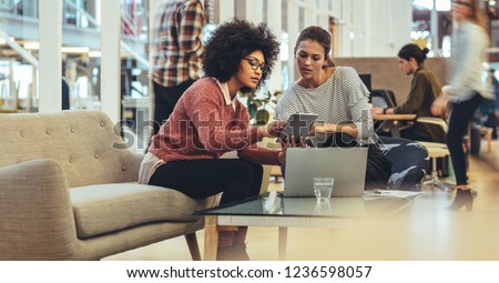 Women entrepreneurs sitting in a lounge at work place sharing ideas using tablet and laptop. Businesswomen in a meeting discussing work in office.