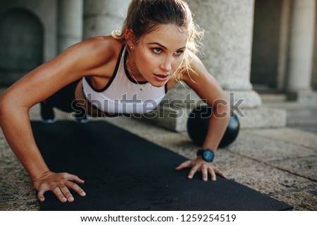 Close up of a woman doing fitness training with a medicine ball by her side. Fitness woman doing push ups on a training mat.