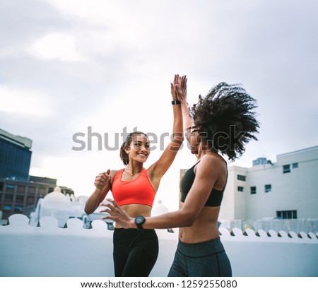 Two cheerful women in fitness wear giving high five while running on the terrace. Women athletes doing fitness training on the rooftop giving high five.