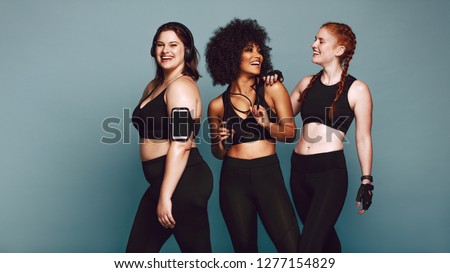 Multi-ethnic group of women together against grey background and smiling. Diverse group females in sportswear after workout.