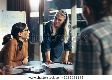 Senior business woman explaining business matters to her team in a boardroom. Mature manager planning new strategy with colleagues in meeting.