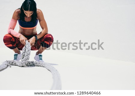 Fitness woman taking a break from workout sitting on her toes holding battle ropes. Woman in fitness wear relaxing during workout.