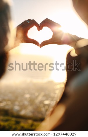 Close up of young couple in love making a heart with their fingers in bright sunlight. Romantic couple gesturing a finger heart.