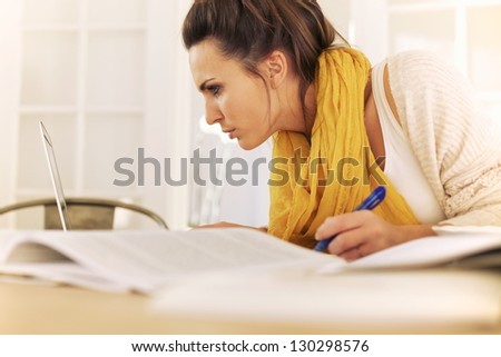 College student reading something in laptop screen and writing it down on her notes