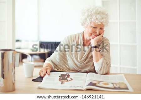 Elegant grandmother sitting at home reading a magazine