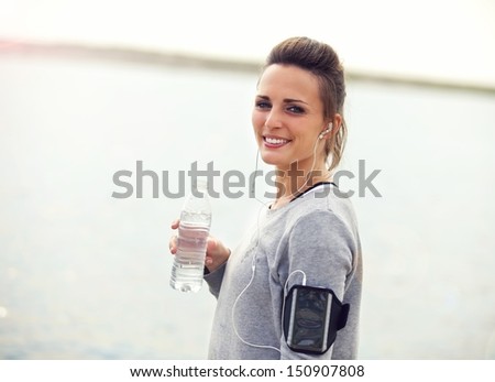 Smiling female water on a running break holding bottled water