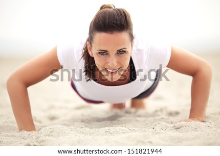 Happy Fitness Caucasian Woman On The Beach Smiling While Doing Push Up Exercise. Active And Healthy Lifestyle.