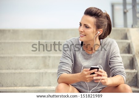 Happy attractive athlete sitting and listening to mp3 music while resting
