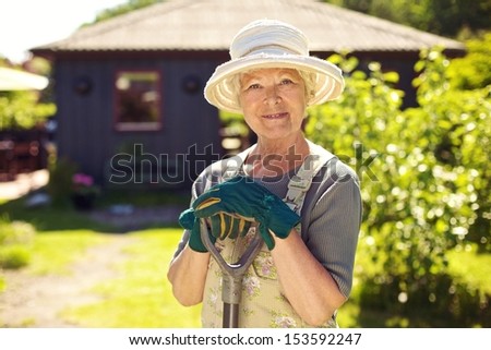 Portrait of elder woman with gardening tools outdoors. Senior woman standing with shovel in her backyard