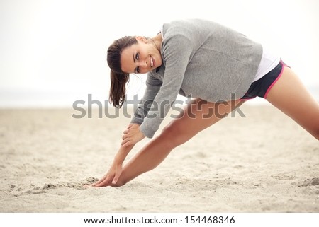 Outdoor female athlete doing her morning stretching and yoga exercise on the beach while smiling and looking happy.