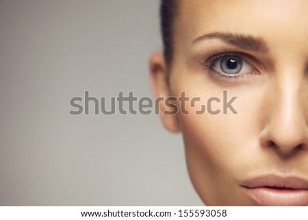 Close-Up Portrait Of Pretty Young Woman With Perfect Healthy Skin And Beautiful Eyes. Half Face Of Pretty Young Female Against Gray Background