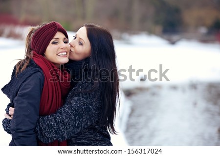 Woman giving her friend a friendly kiss on the cheek outdoors