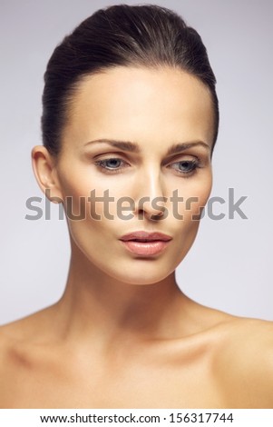 Closeup portrait of beautiful young lady with natural makeup looking down. Pretty female model posing against gray background