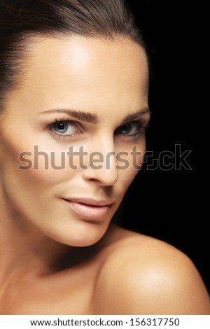 Close-up portrait of a attractive young female with flawless skin looking at camera. Pretty woman with clean and glowing skin isolated on black background