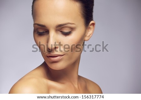 Portrait of pretty young woman looking down at her beautiful shoulders against gray background. Sensual young female posing in gray background