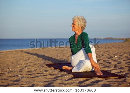 Senior woman performing a yoga routine on the beach. Elder woman doing stretching exercise on sandy beach with lots of copyspace