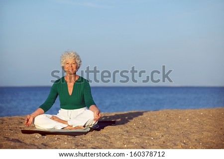 Portrait of the senior woman meditating on the seashore with lots of copyspace. Elder woman doing relaxation exercise on sandy beach during morning.