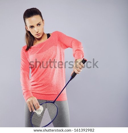 Portrait of attractive young woman with badminton racket ready to serve. Female badminton player playing against grey background