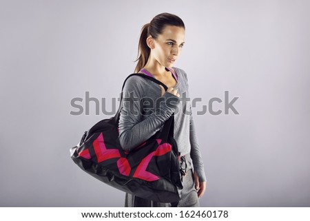 Portrait of fit young woman carrying gym bag looking away at copyspace over grey background. Beautiful caucasian female ready for gym exercise.