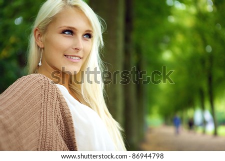 Face of an attractive confident self-assured young blonde woman in a tree-lined park avenue.