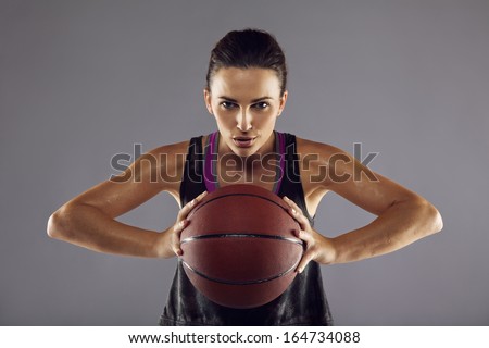 Portrait of happy female basketball player passing the ball. Beautiful young woman in sportswear holding basketball looking at camera against grey background