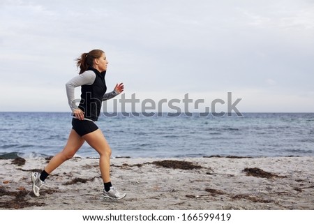 Fit and healthy young woman running along shoreline. Caucasian female athlete exercising running on beach. Beautiful young woman runner running on beach.