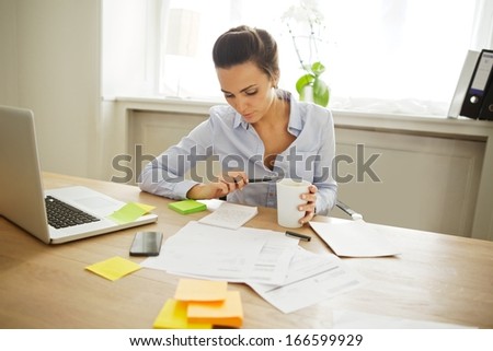 Attractive young woman working at the desk with sticky notes and laptop. Beautiful businesswoman reading notes while sitting in home office.