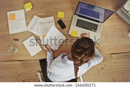 High Angle View Of An Young Brunette Working At Her Office Desk With Documents And Laptop. Businesswoman Working On Paperwork.