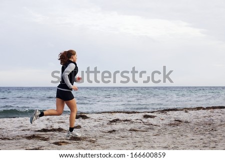 Young female athlete jogging during outdoor workout on beach. Fit and beautiful young woman running. Female runner going outdoor workout on seashore.