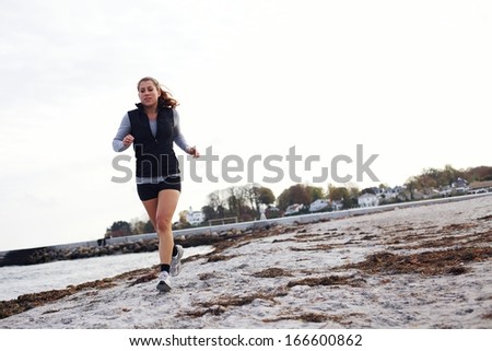 Young woman jogging along beach wearing sports clothing. Healthy female running on sea shore. Female runner exercising outdoors