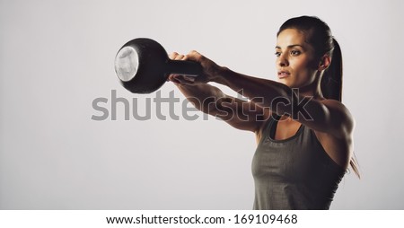 Young Fitness Female Exercise With Kettle Bell. Mixed Race Woman Doing Crossfit Workout On Grey Background. Kettlebell Swing.