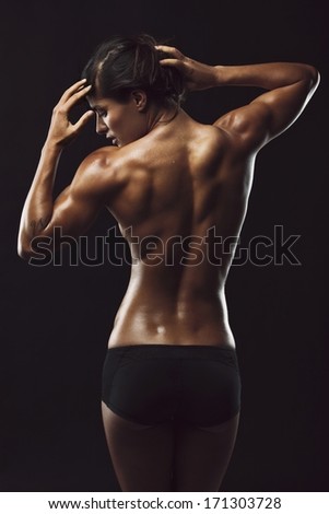 Rear View Of Fit Young Woman Bodybuilder Posing With Naked Back On Black Background. Muscular Female With Perfect Body.