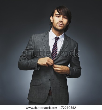 Portrait of handsome young male model buttoning coat. Attractive businessman getting dressed. Mixed race male model on black background.